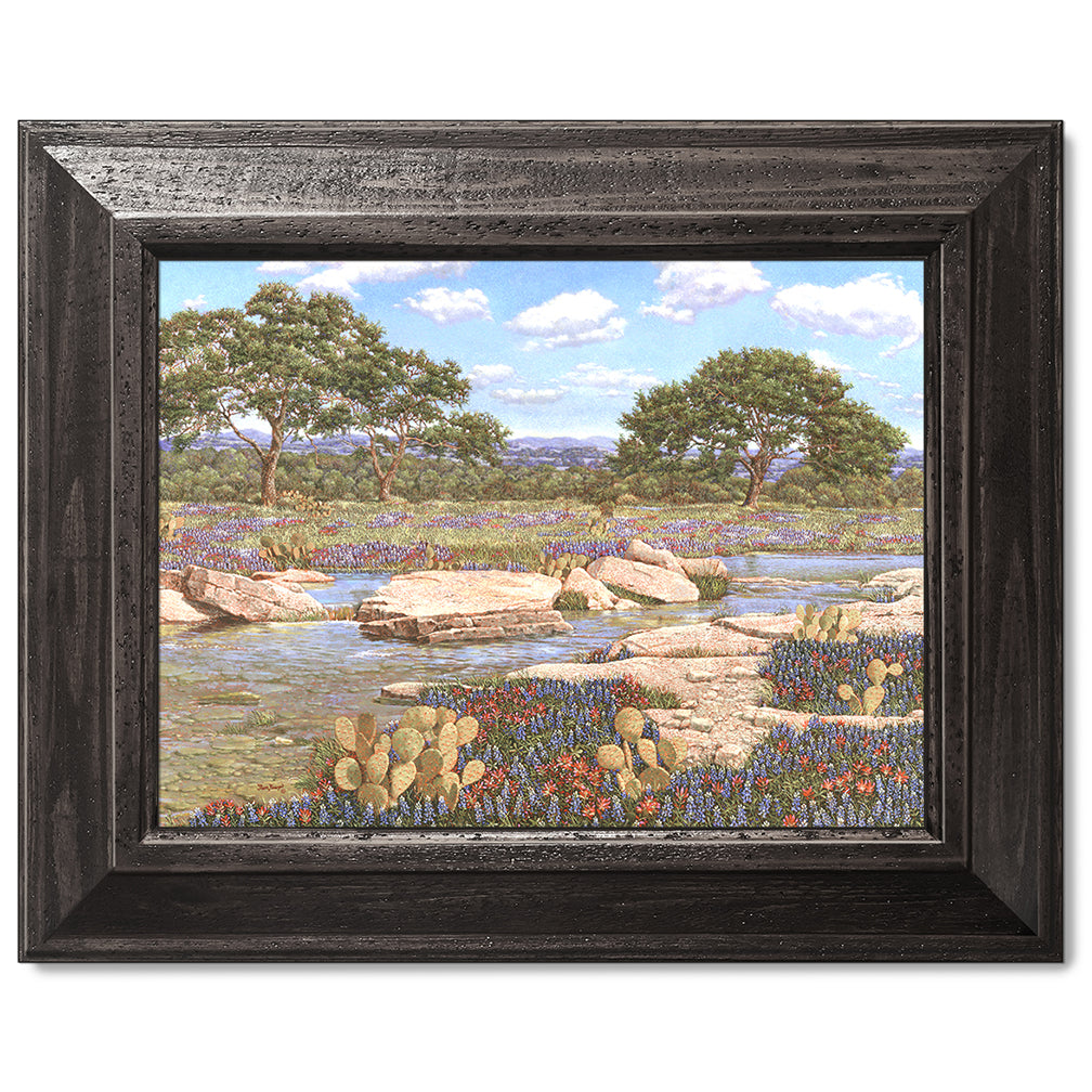 canvas print in a black wood frame depicting a country creek
landscape with the wildflowers bluebonnets and Indian paintbrushes