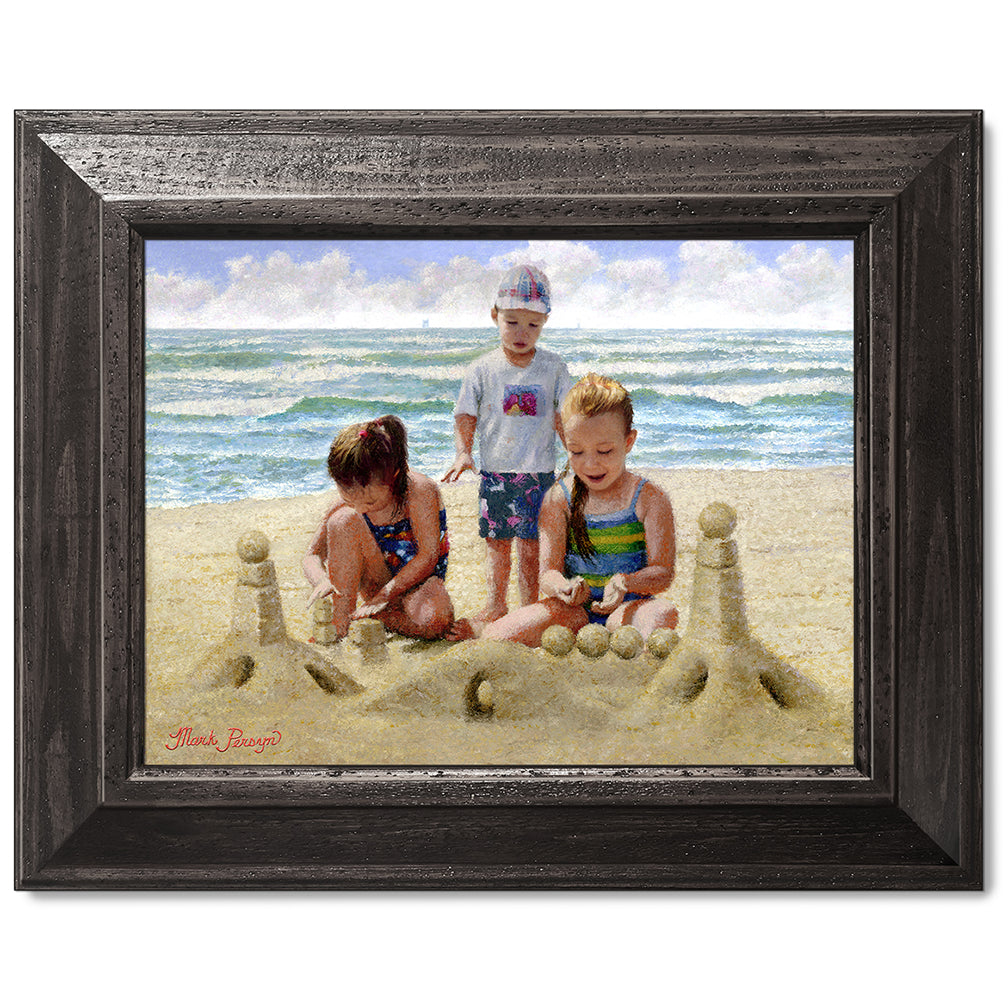 canvas print in a black wood frame depicting children building
a sandcastle on a beach with waves in the background