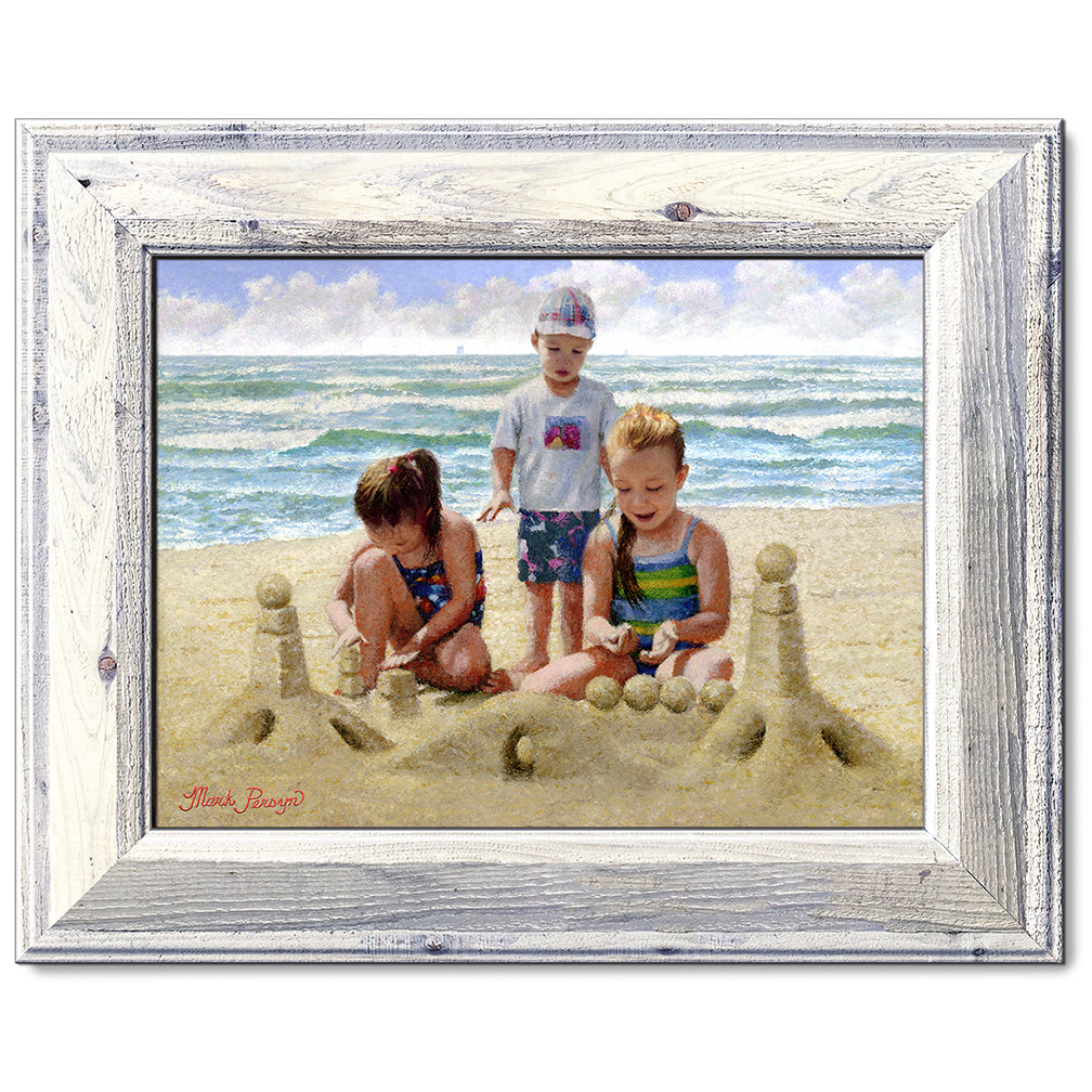 canvas print in a whie wood frame depicting children building
a sandcastle on a beach with waves in the background