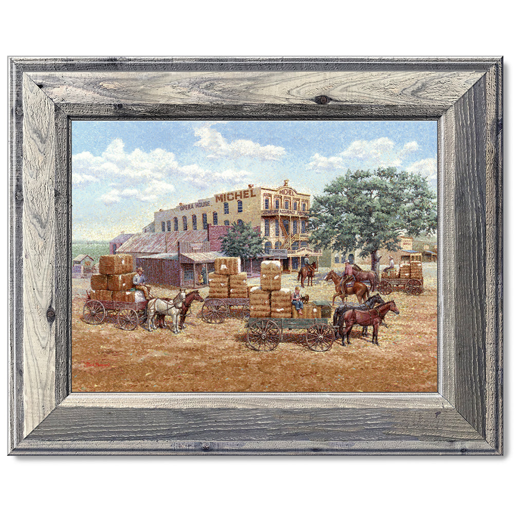 canvas print in a grey wood frame depicting a main street in a 
western town with cotton wagons hauling large cotton bails