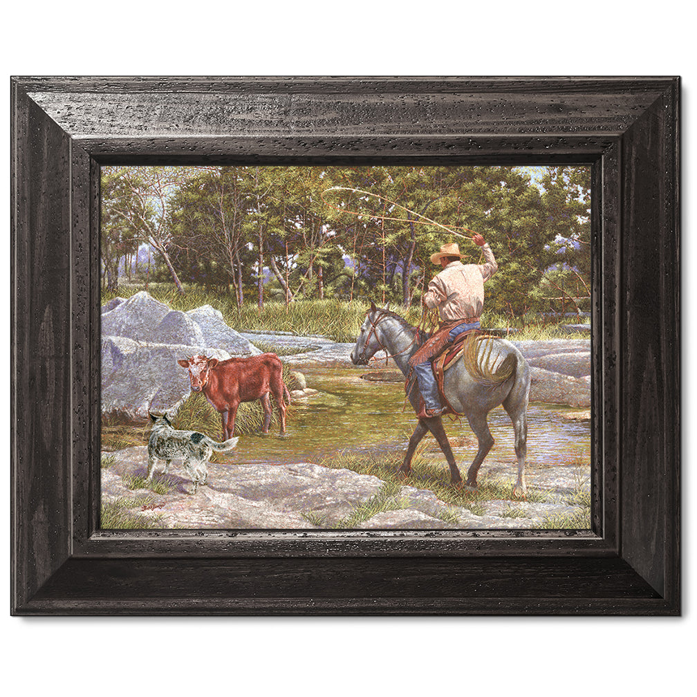 canvas print in a black wood frame depicting a cowboy on 
horseback roping a calf in a creek with his blue healer dog  