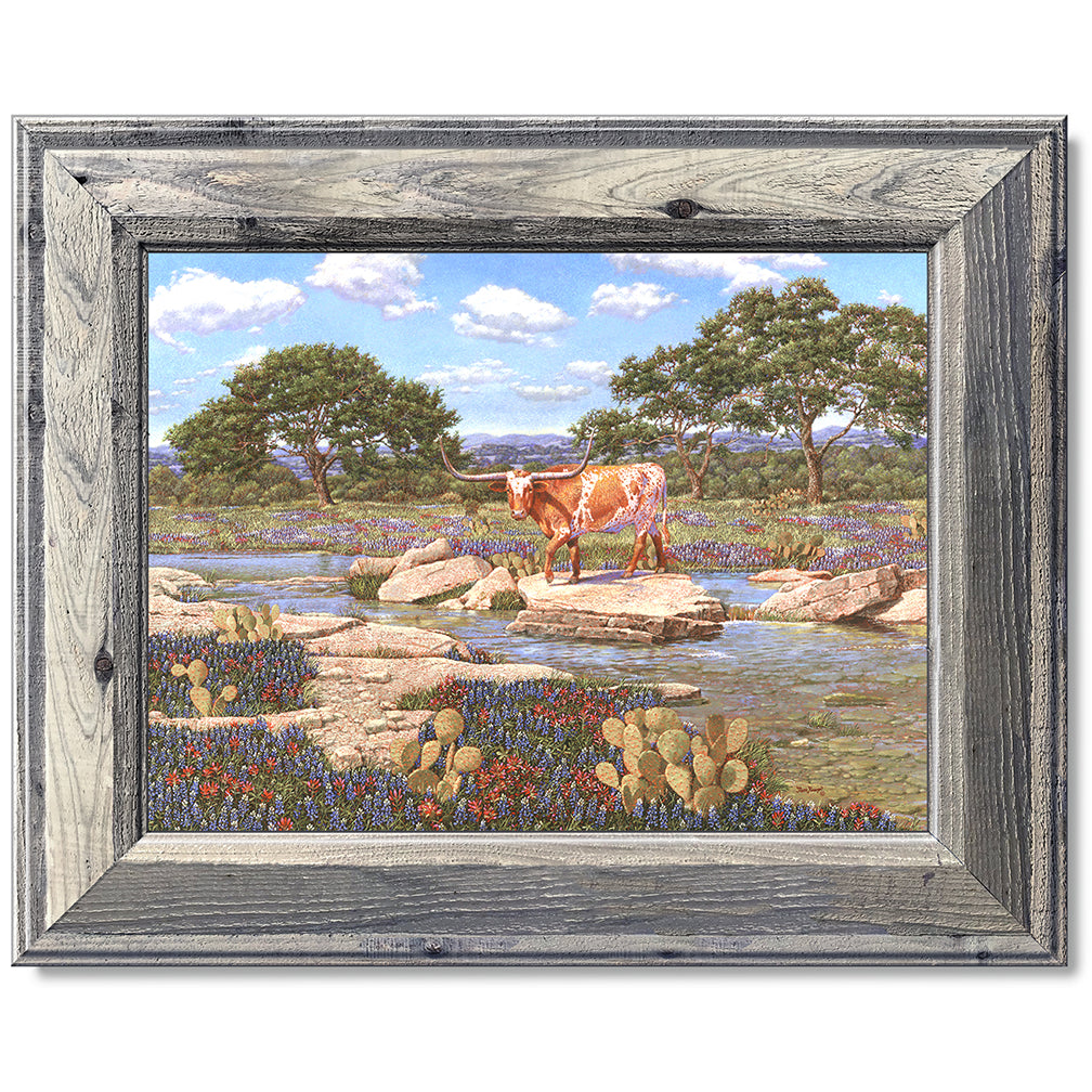 canvas print in a grey wood frame depicting a longhorn near a
creek with the wildflowers bluebonnets and Indian paintbrushes