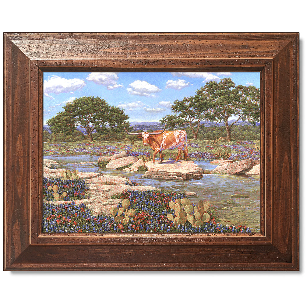 canvas print in a brown wood frame depicting a longhorn near a
creek with the wildflowers bluebonnets and Indian paintbrushes