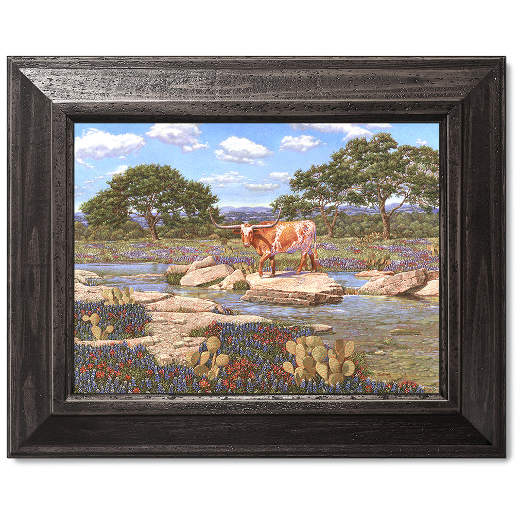 canvas print in a black wood frame depicting a longhorn near a
creek with the wildflowers bluebonnets and Indian paintbrushes