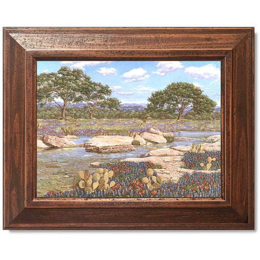 canvas print in a brown wood frame depicting a country creek landscape with the wildflowers bluebonnets and Indian paintbrushes 